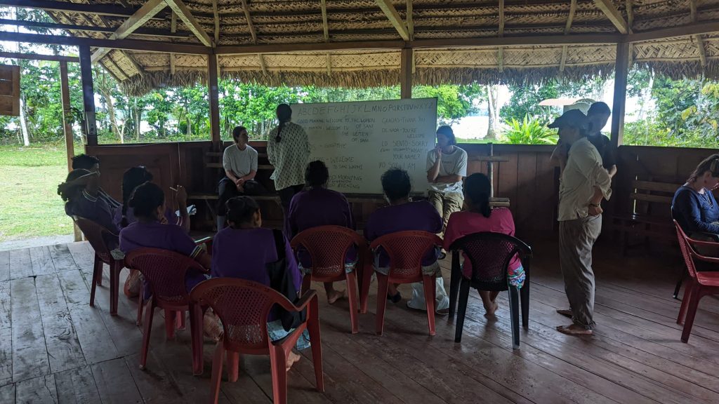 Indigenous people sit around a whiteboard as other people teach them English